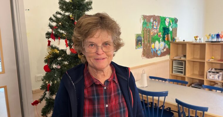 Kvinna i rutig skjorta och lockigt hår framför en julgran på en förskola.