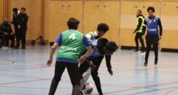Några spelare kämpar om bollen i en fotbollsmatch i en idrottshall.