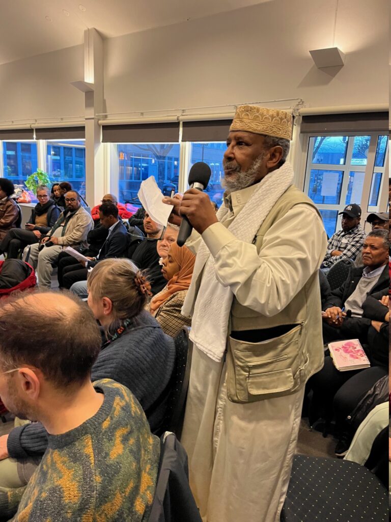 En äldre muslimsk man står upp i publiken och pratar i mikrofon.