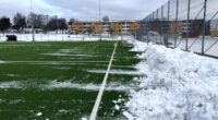 En grön plastgräsplan med snövallar längs sidorna.