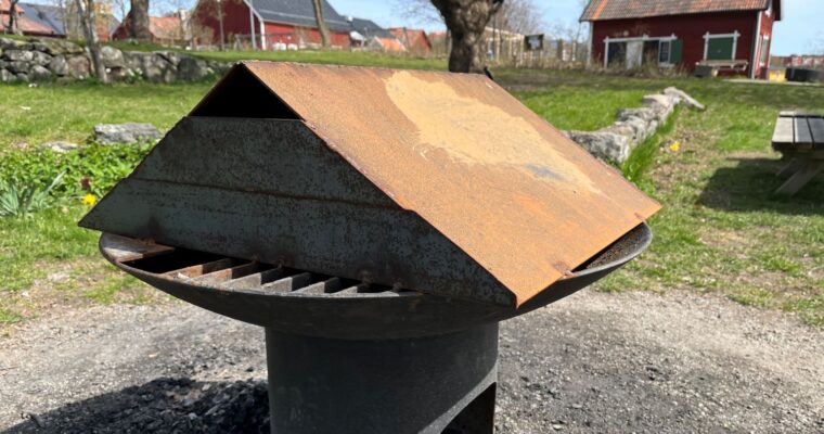 allmän grillplats med stålskal över sig framför röda stugor