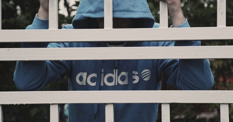 man i adidasluvtröja står bakom ett vitt galler