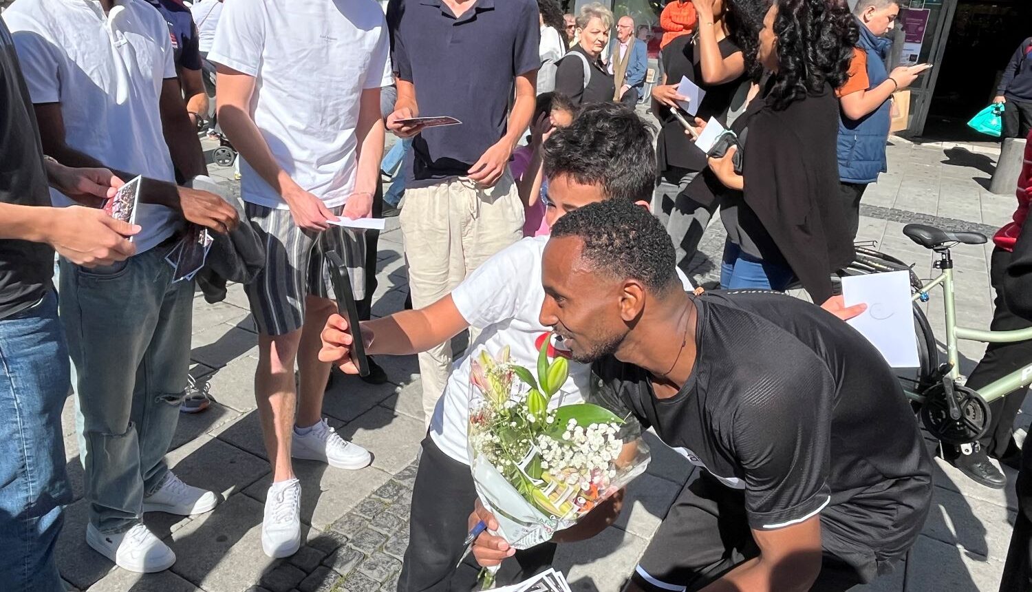 SM-vinnaren Habtom Asgede tar selfie med yngre beundrare på ett torg