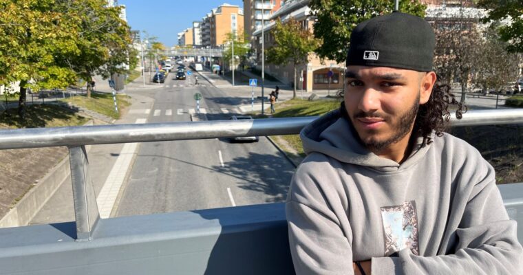 man står med armarna i kors på en bro över Rinkebystråket och tittar in i kameran