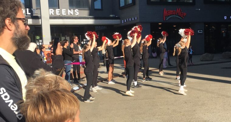 några cheerleaders i svarta kläder står framför publik under ett lopp