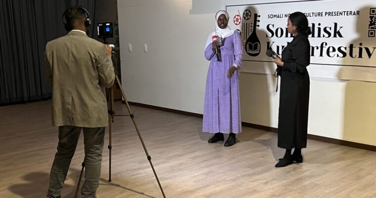 två kvinnor samtalar under en intervju på scen och filmas av en man med stativ