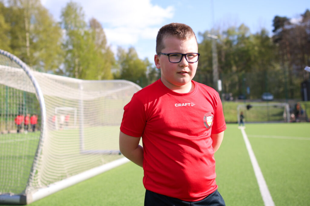 ung kille i fotbollskläder står på en bollplan