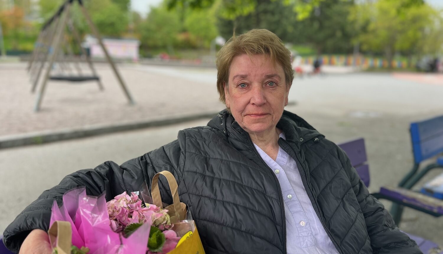 Yvonne på en parkbänk med kasse blommor bredvid sig.