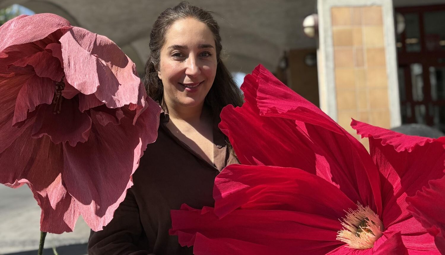 kvinna står mitt emellan en stor rosa och en stor cerise pappersblomma