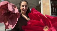 kvinna står mitt emellan en stor rosa och en stor cerise pappersblomma