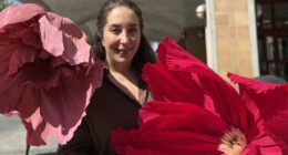 kvinna står mitt emellan en stor rosa och en stor cerise pappersblomma
