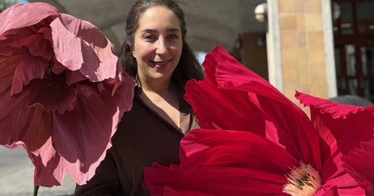 kvinna står mitt emellan en stor rosa och en stor cerise pappersblomma