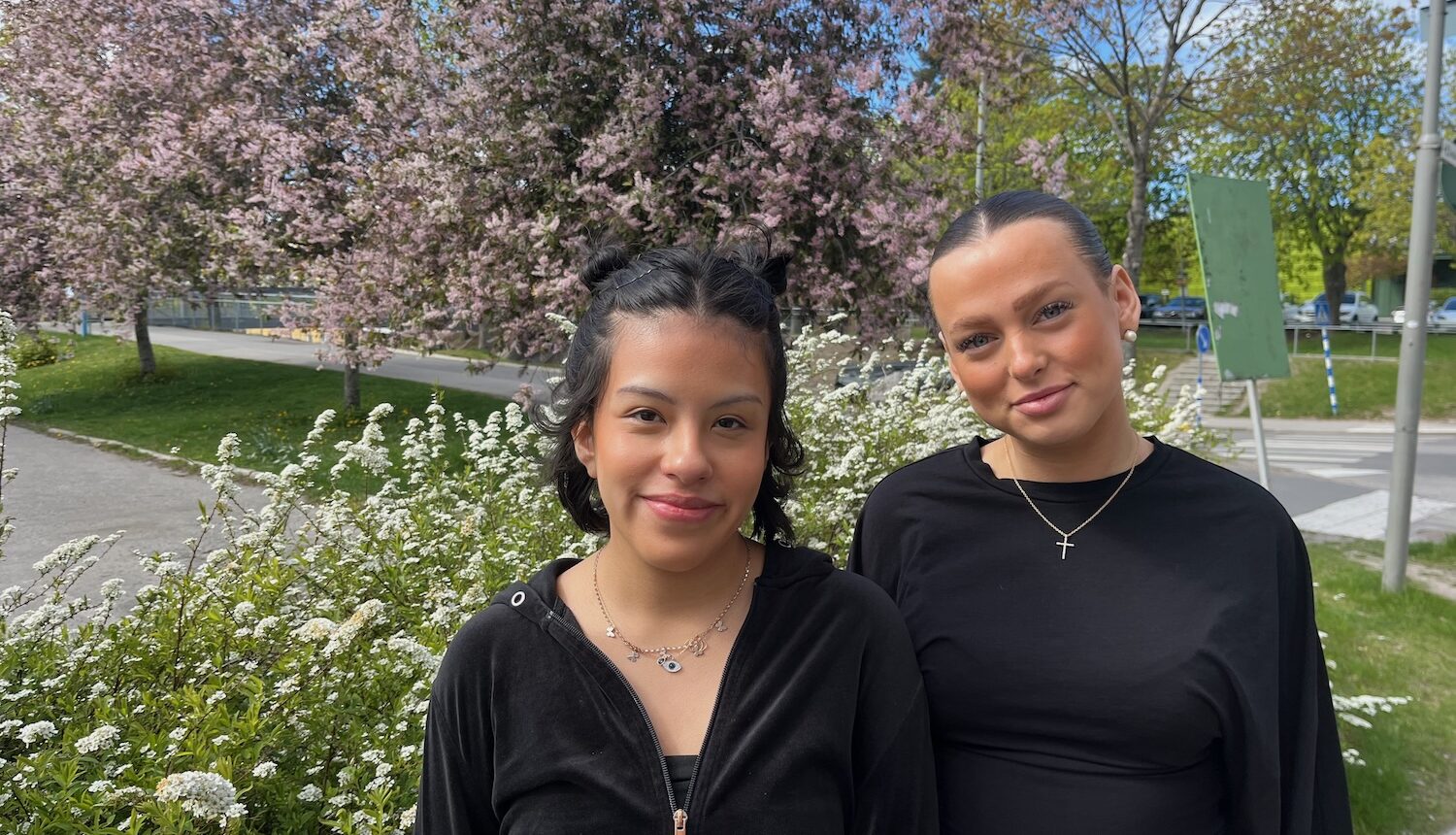 Två leende unga kvinnor fram blommande träd.