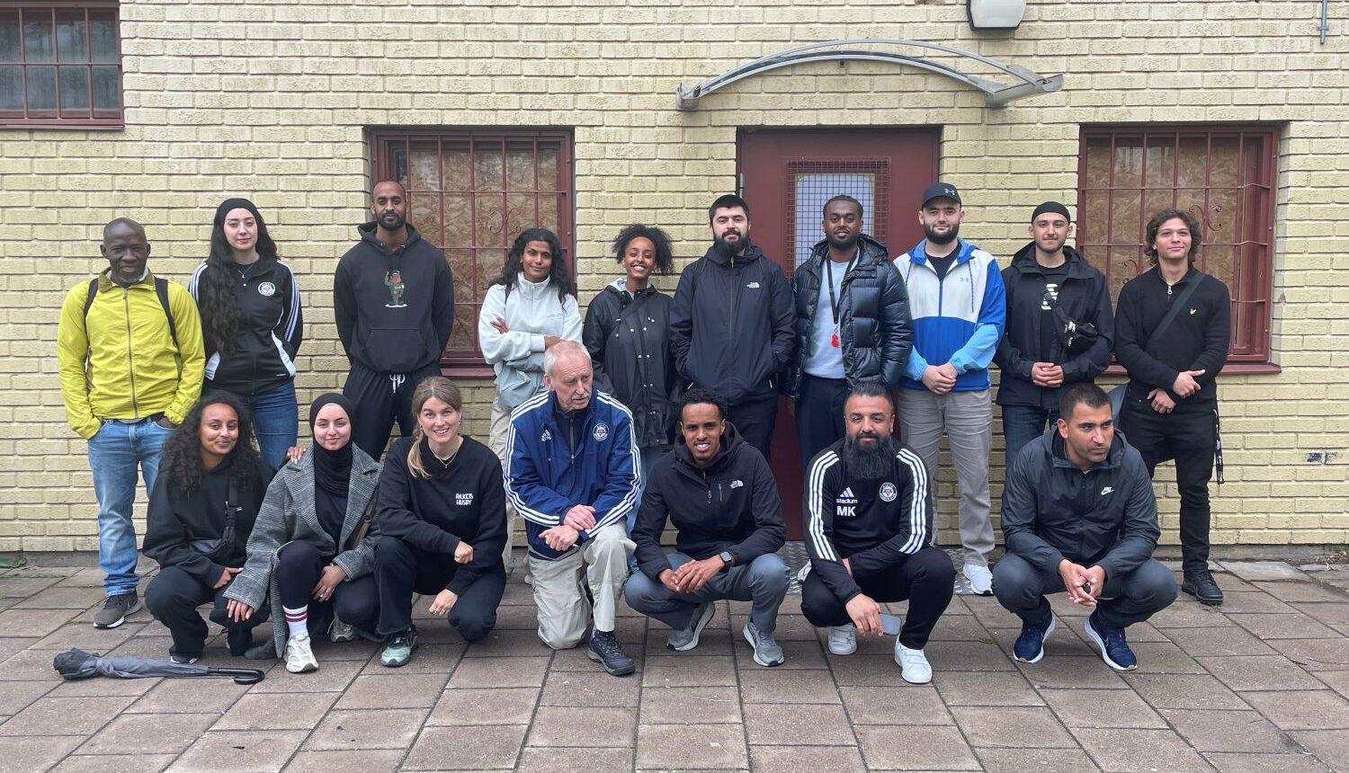 gruppbild av föreningsrepresentanter framför gul tegelbyggnad