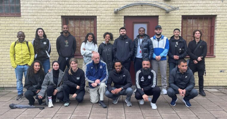 gruppbild av föreningsrepresentanter framför gul tegelbyggnad