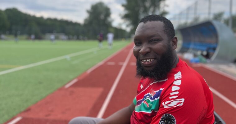 Babou sitter vid planen i röd matchtröja.