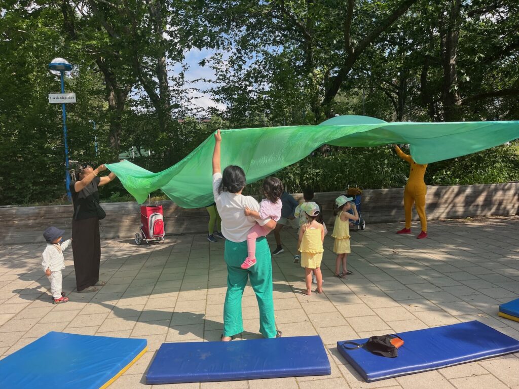 Barn och skådespelare lekte tillsammans med ett stort grönt tyg.