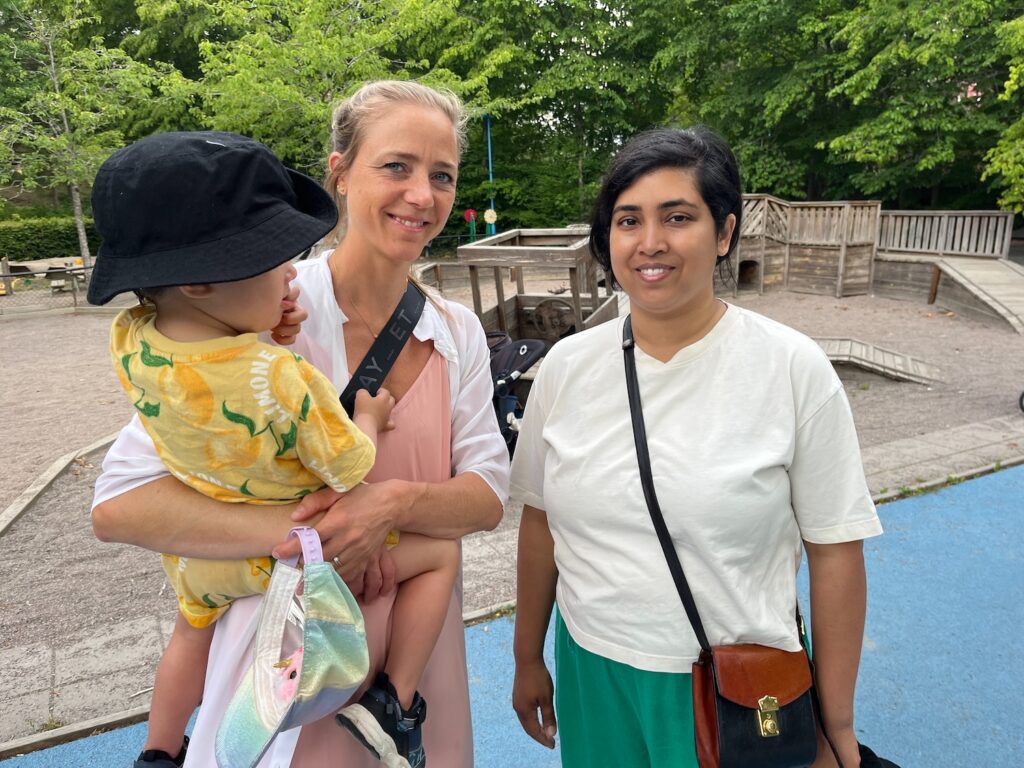 Två kvinnor bredvid varandra, den ena har ett barn i famnen.