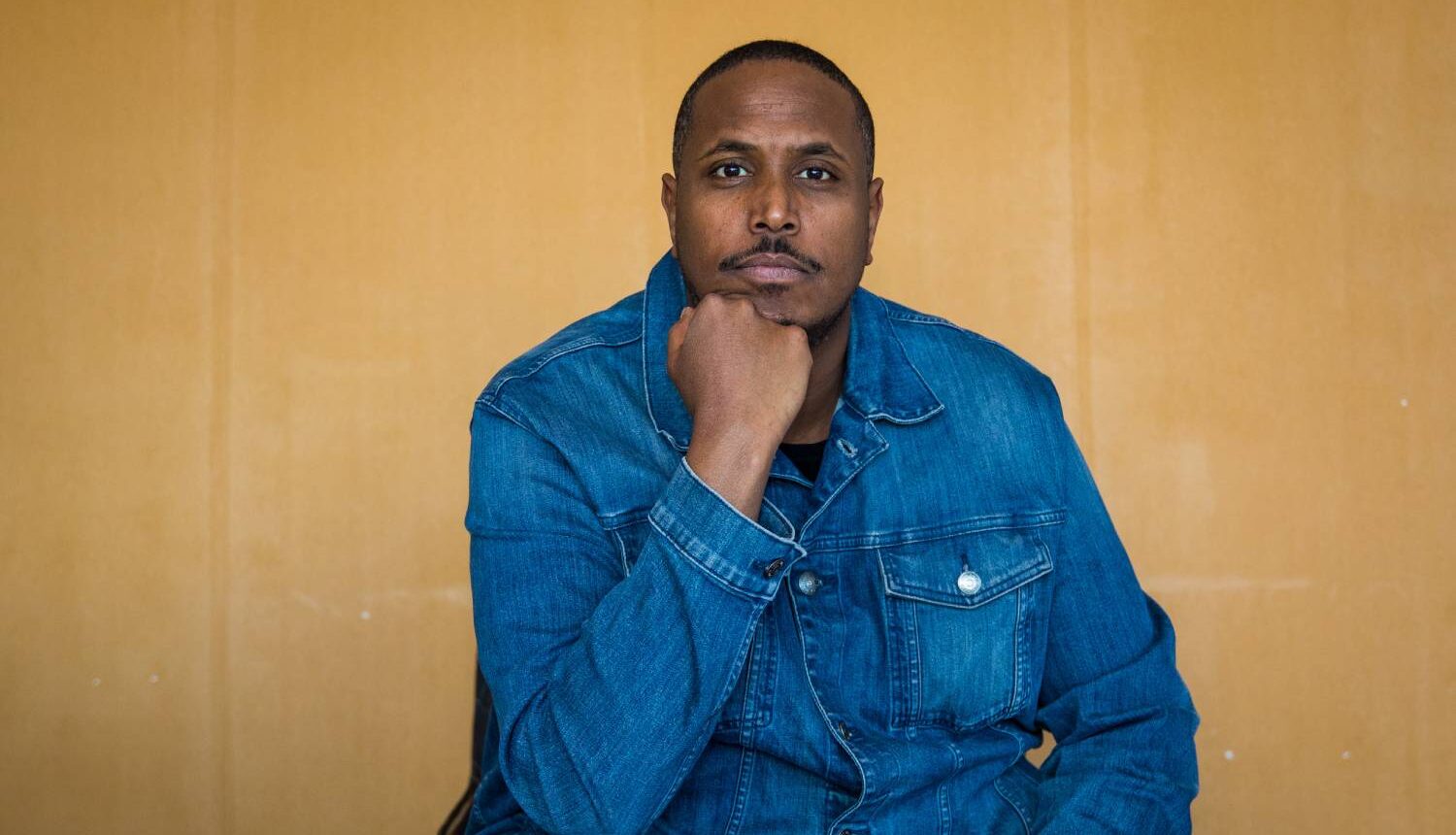 En svart man som sitter, vilar huvudet på handen, och ser rakt in i kameran.