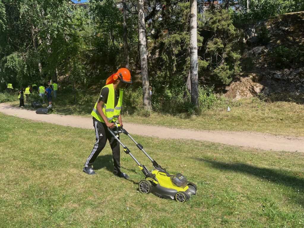 Kille i hjälm, hörselkåpor och visir som klipper gräs.