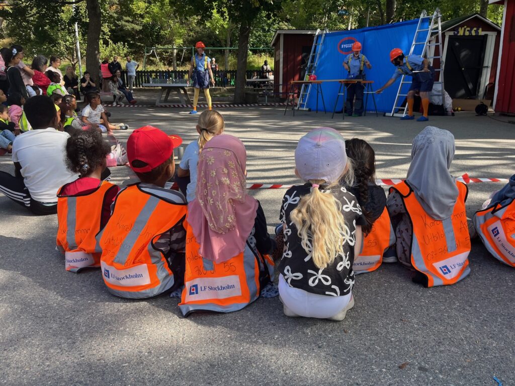 Man ser clownerna, men bilden är tagen bakom fem sex barn som sitter på marken.