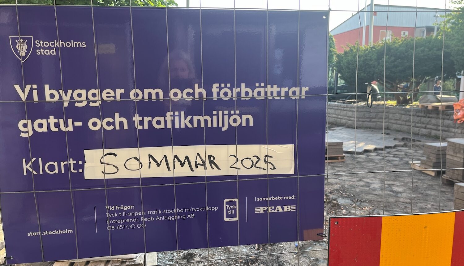 En skylt som säger att ombyggnaden av Hjulsta torg ska vara klar sommaren 2025. Bakom stängslet ser man att så inte är fallet.