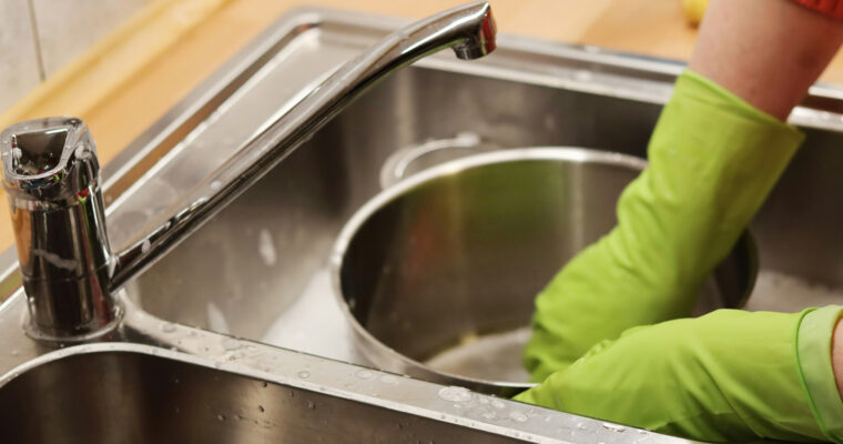 Händer med handskar som diskar en kastrull för hand