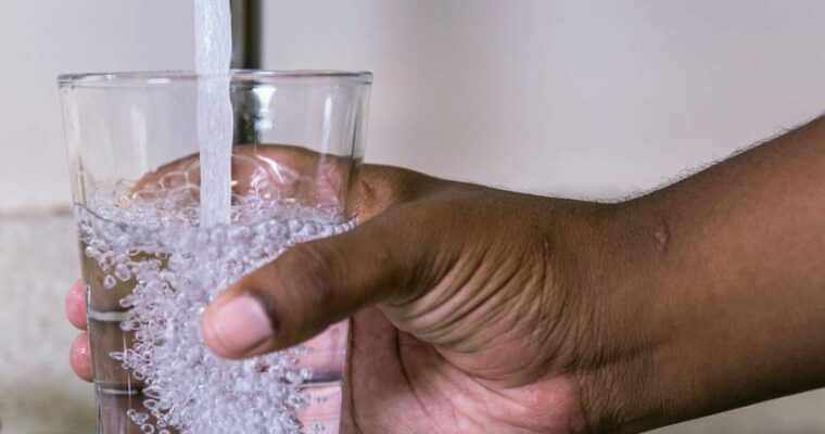 En hand som håller ett glas under vattenkranen.