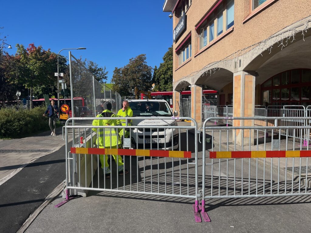 Gatan avstängd med stängsel, tre arbetare i gula varseljackor.
