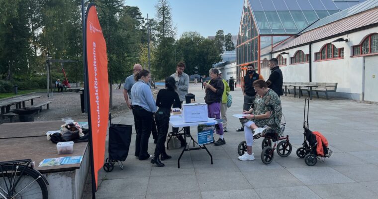 En stående vimpel från stadsdelsförvaltningen och några människor runt ett bord.