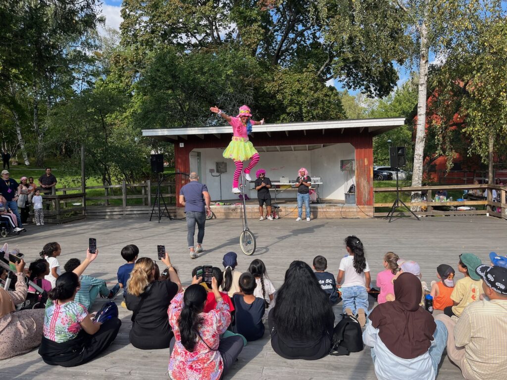 En clown högt upp på en gigantisk enhjuling.