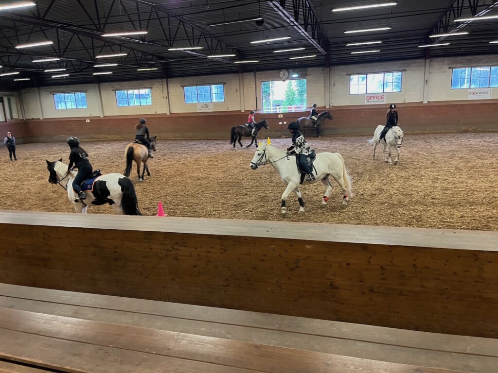 Hästar med ryttare i en inomhusmanege.