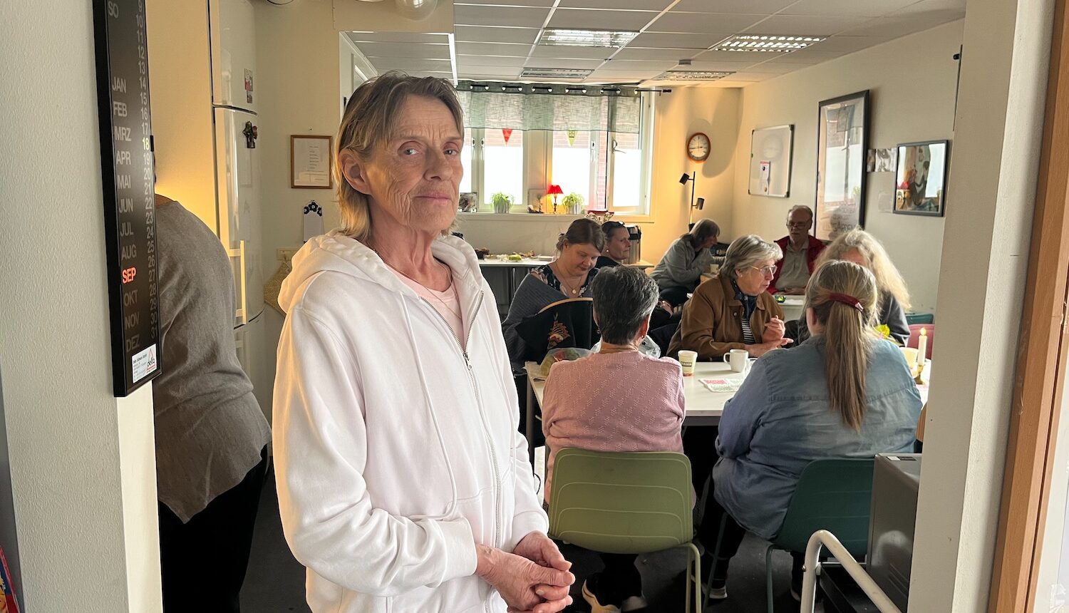 Pia står i ingången till ett rum där många sitter och fikar.