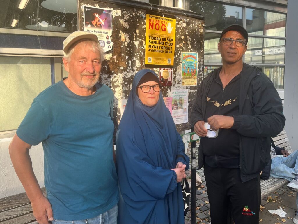 två män och en kvinna står framför en protestaffisch