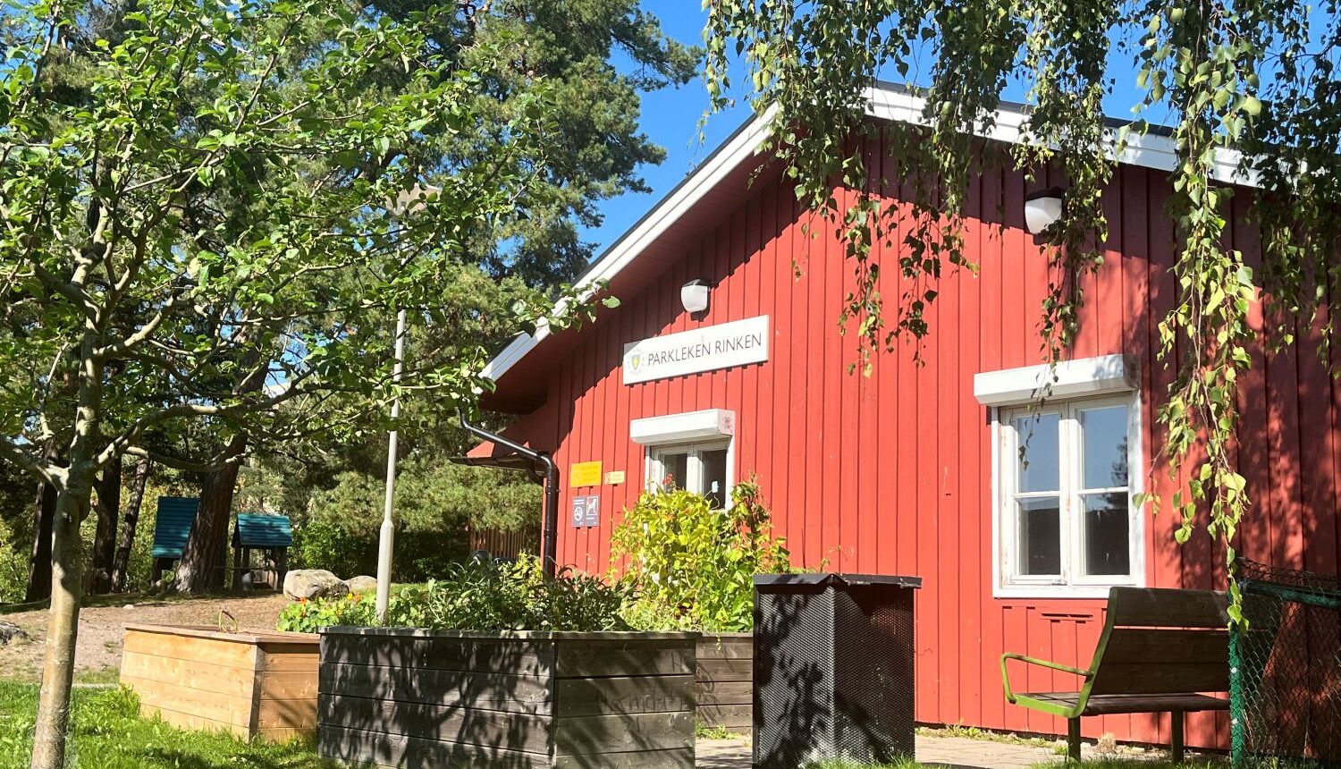 det röda parklekshuset rinken i solsken och omgiven av grönska