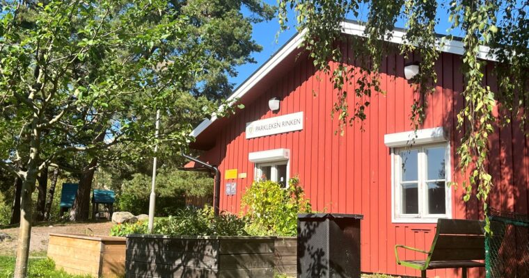 det röda parklekshuset rinken i solsken och omgiven av grönska