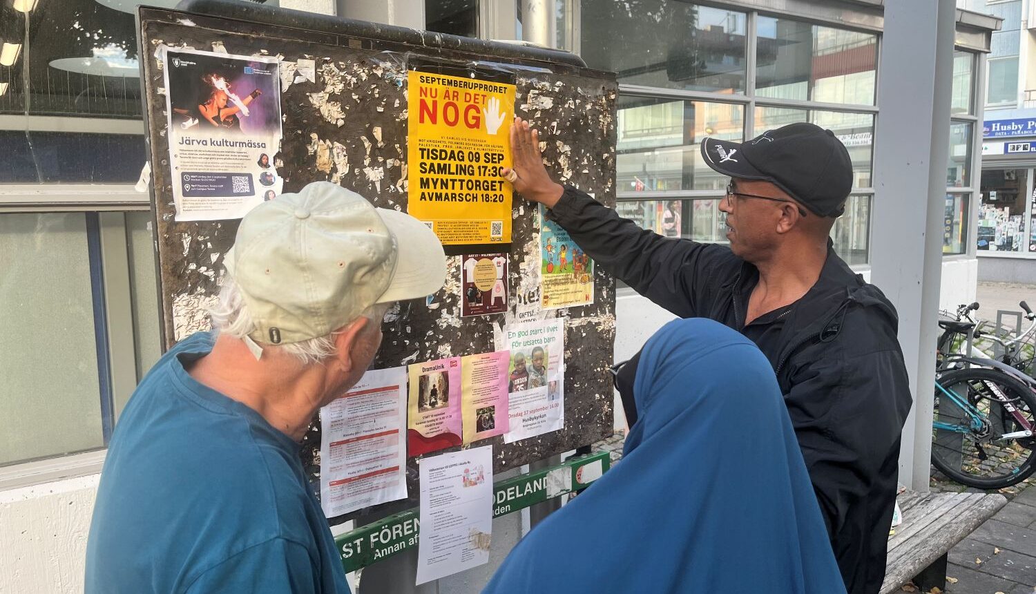 tre personer sätter upp en protestaffisch på en anslagstavla