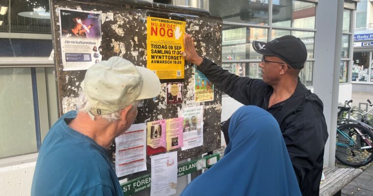tre personer sätter upp en protestaffisch på en anslagstavla