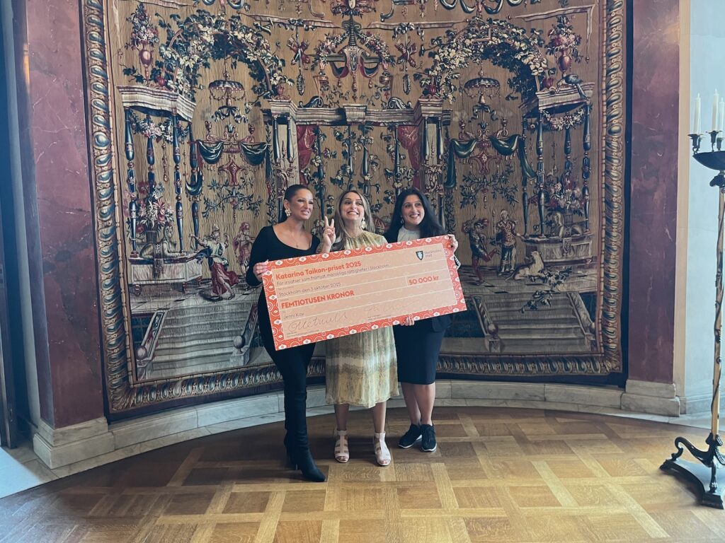 Tre kvinnor bakom en jättestor check med 50 000 kr skrivet på.