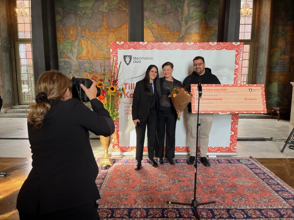 Två kvinnor och en man med en gigantisk prischeck, en kvinnlig fotograf tar bilder.