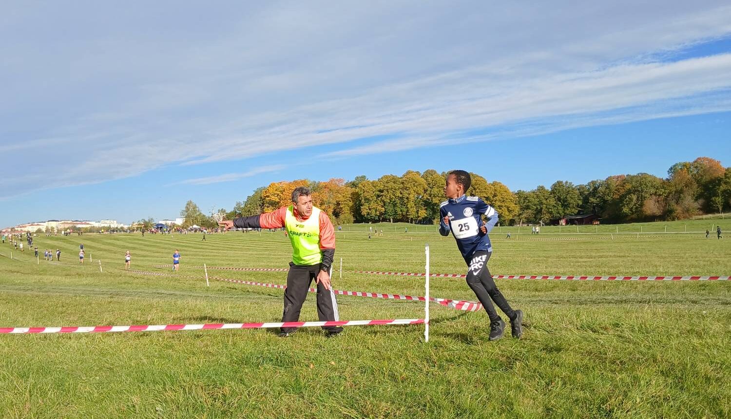En pojke springer på ett stort fält och en funktionär visar vägen.