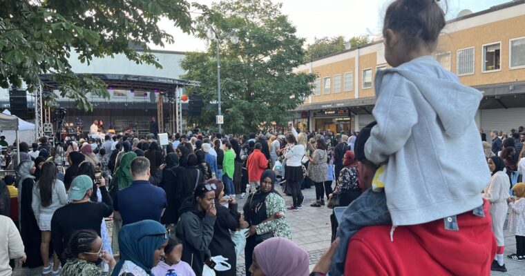 ett barn sitter på en vuxens axlar och tittar mot ett folkhav framför en scen