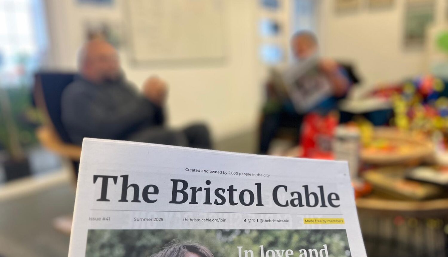 Tidningen i förgrunden och två män suddigt i bakgrunden.