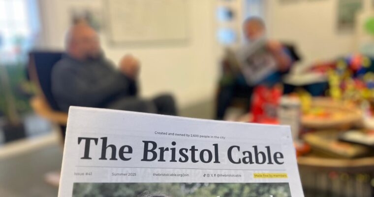 Tidningen i förgrunden och två män suddigt i bakgrunden.