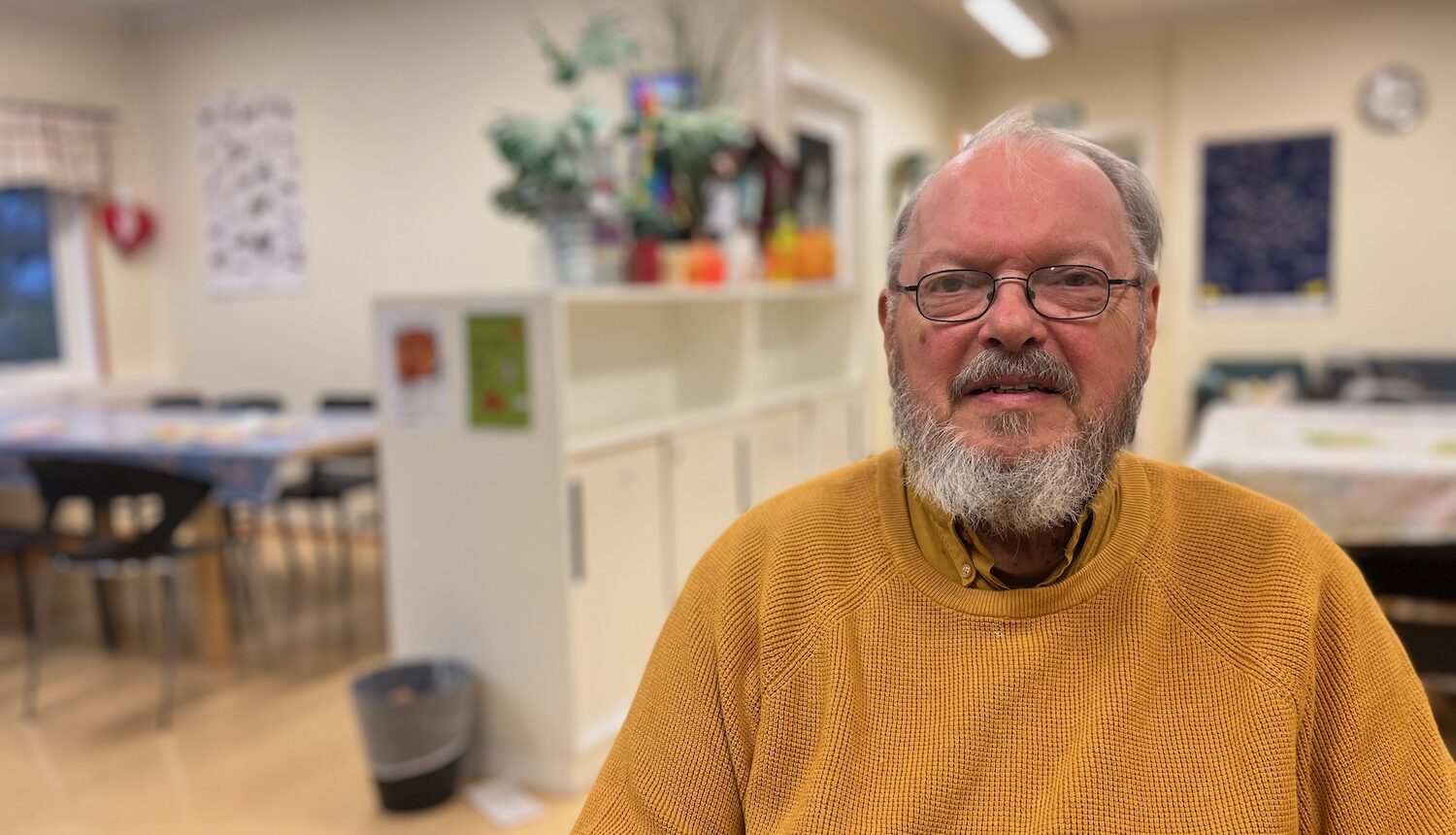 En äldre man i senapsgul tröja sitter inne i Erikslunds parklek.