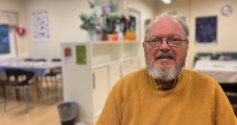 En äldre man i senapsgul tröja sitter inne i Erikslunds parklek.