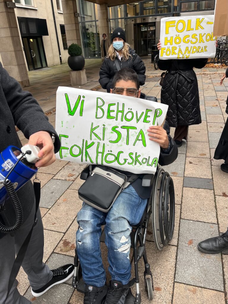 En av deltagarna i rullstol med ett plakat "Vi behöver Kista folkhögskola".