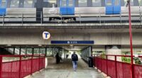 en gångbro under tunnelbanebro där ett tåg passerar utomhus
