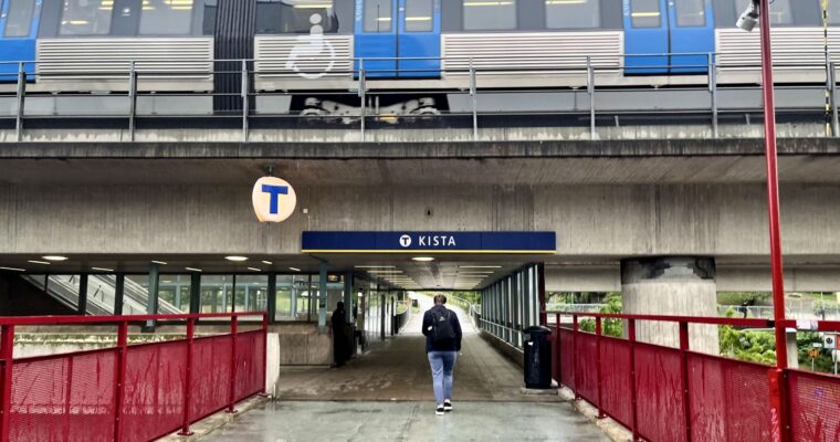 en gångbro under tunnelbanebro där ett tåg passerar utomhus