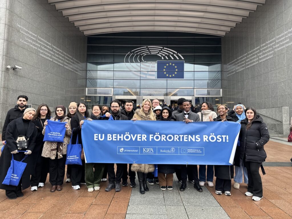 En stor grupp deltagare från Kista och Botkyrkas folkhögskolor bakom en blå banderoll där det står: EU behöver förortens röst.